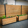 Two 18" x 60" cedar planter boxes with black steel corners placed on a patio, filled with flowers and herbs, set against a wooden privacy fence.